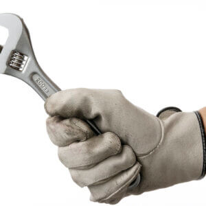 A worker's gloved hand holding a wrench.