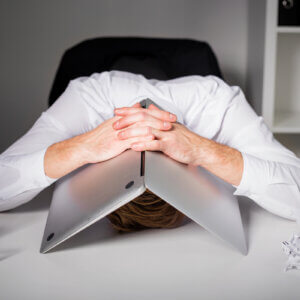 Man with head on desk covered by his laptop